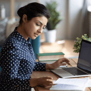 A focused woman working on a laptop at a desk with documents, projecting concentration and professionalism in an office setting.