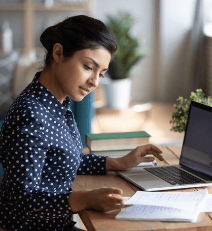 A focused woman working on a laptop at a desk with documents, projecting concentration and professionalism in an office setting.