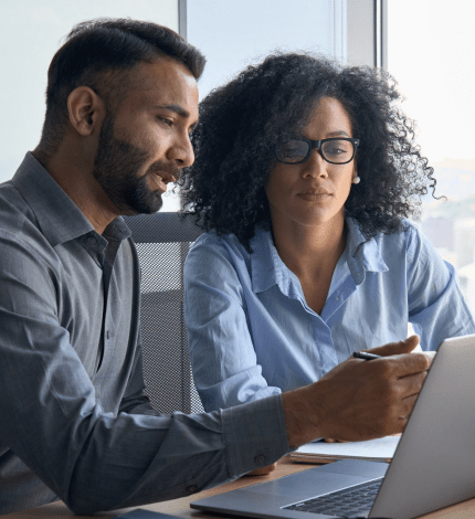 Two professionals collaborating in an office in front of a laptop.