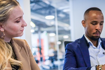 Focused man and woman in professional attire working, with the man typing on a computer in a modern office setting.