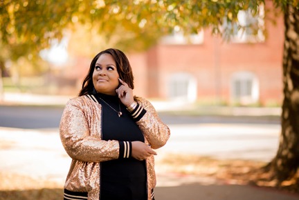 A contemplative Beth Ruffin in a sparkling jacket stands amidst autumn leaves, with a thoughtful expression, gazing into the distance.